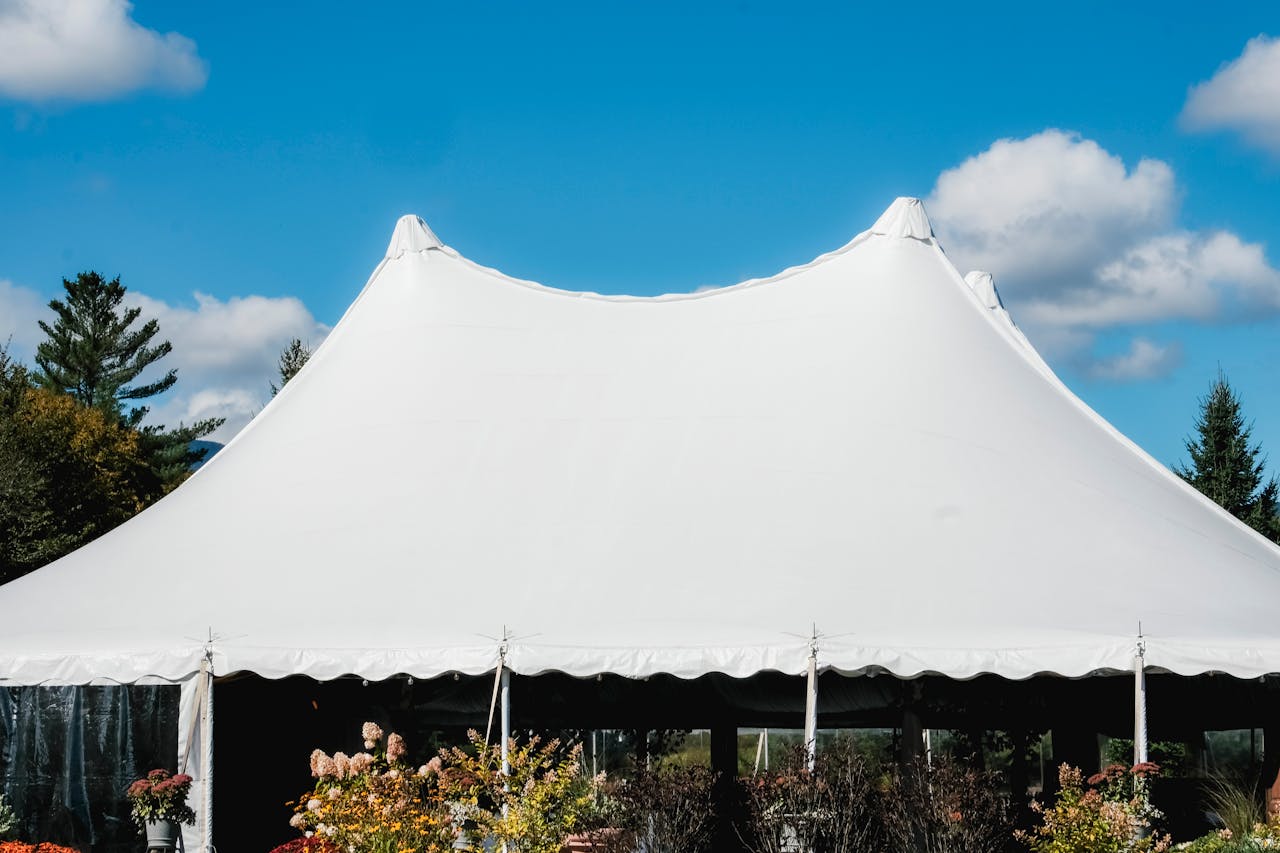 hero-img-01 A sleek white tent set up outdoors under a vibrant blue sky with fluffy clouds.